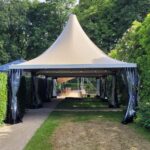 Beige pagodetent van 5×5 meter met hoog puntdak en vier zijwanden, met sterk aluminium frame en PVC doek, geschikt voor feestelijke, particuliere of zakelijke buitengelegenheden.