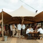 Stretchtent met zandkleurig doek, houten palen en scheerlijnen, te huur bij vanBos tenten.