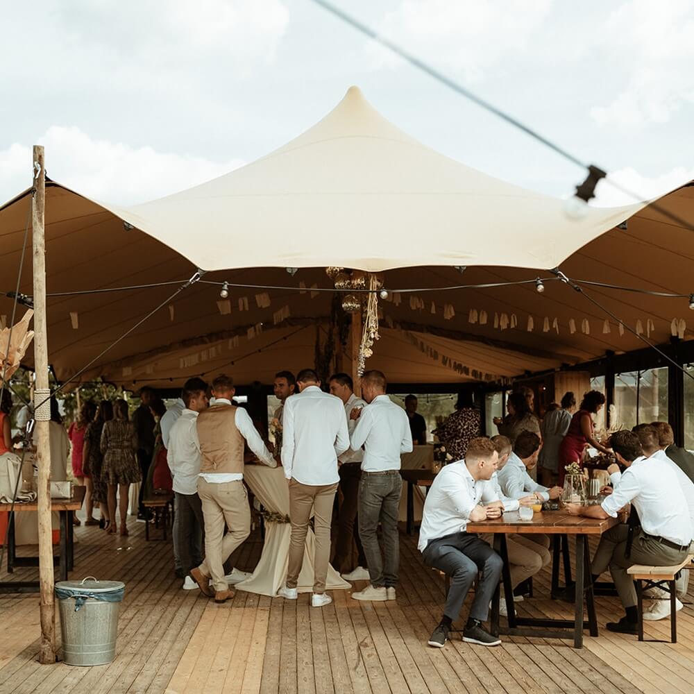Stretchtent met zandkleurig doek, houten palen en scheerlijnen, te huur bij vanBos tenten.